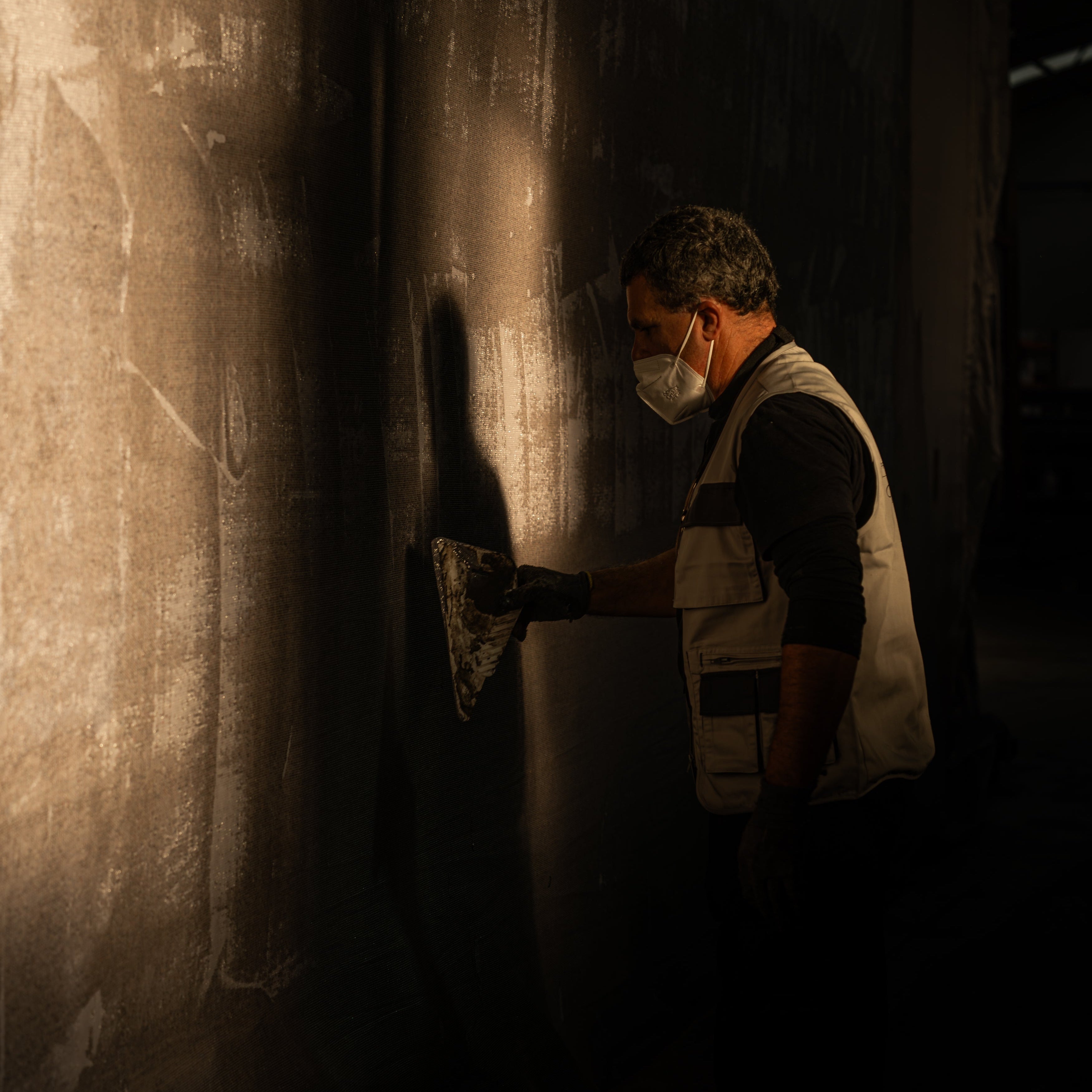 Person sanding a wall in a dimly lit room