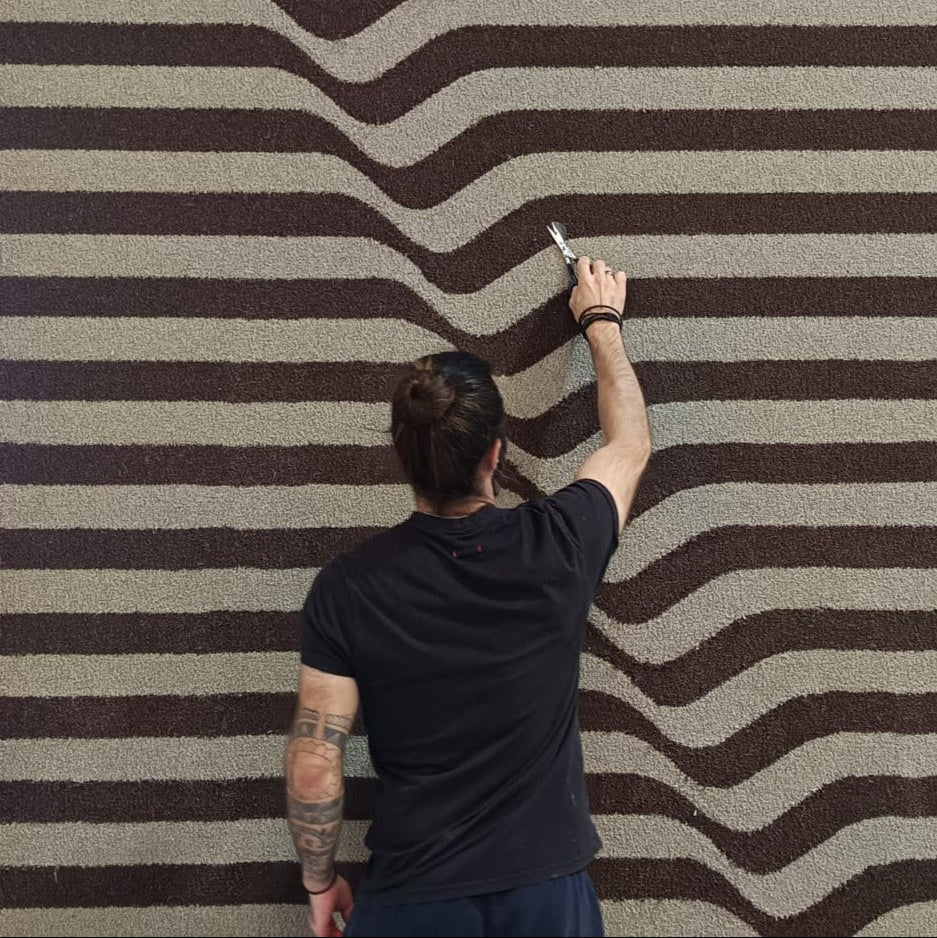 Person drawing wavy lines on a striped wall with a marker.